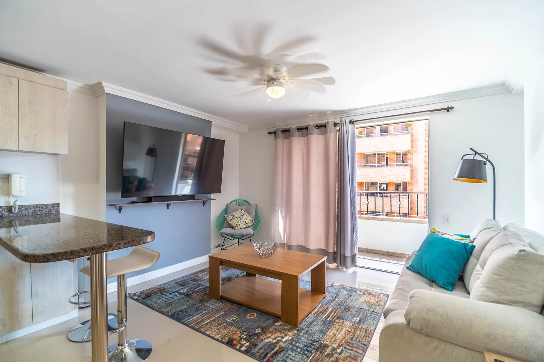 The apartment living room with a white sofa, turquoise cushions and doors onto the balcony
